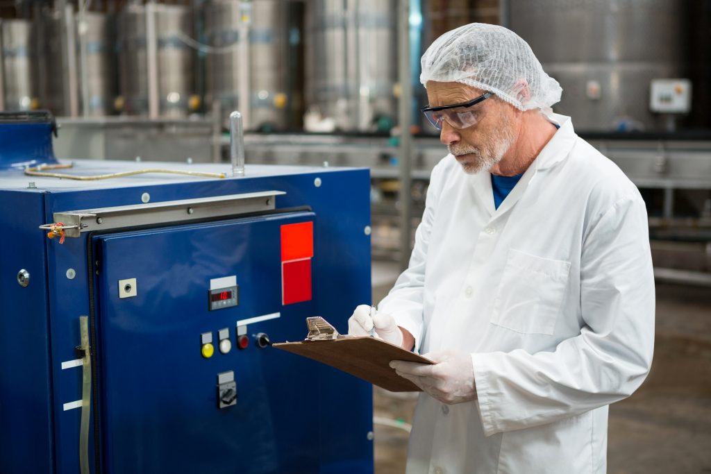 serious male worker inspecting machines at cold drink factory