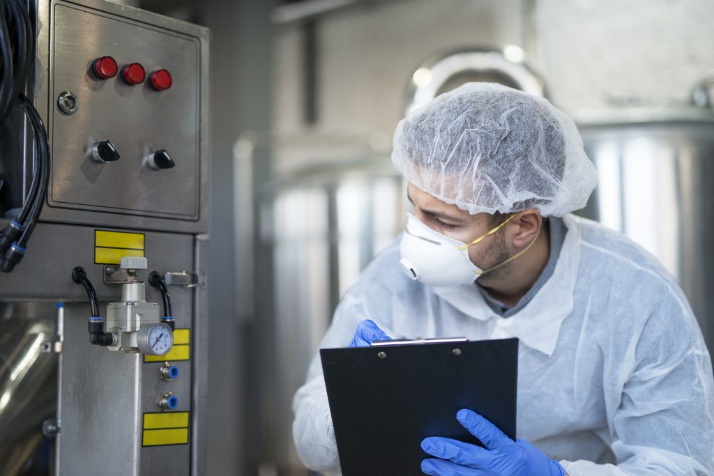 young technologist in white protective uniform controlling industrial machine at production plant.